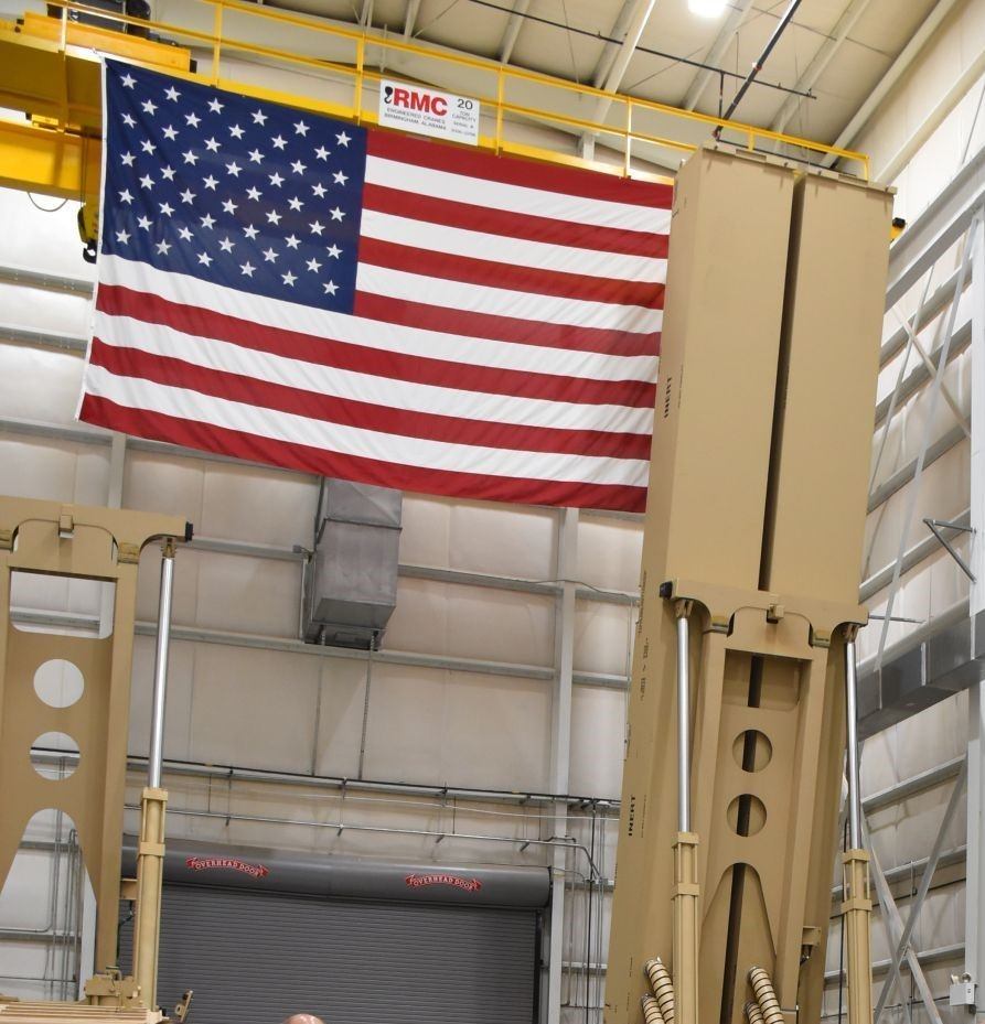 a large American flag hangs from a wall inside a warehouse behind a missile launcher system